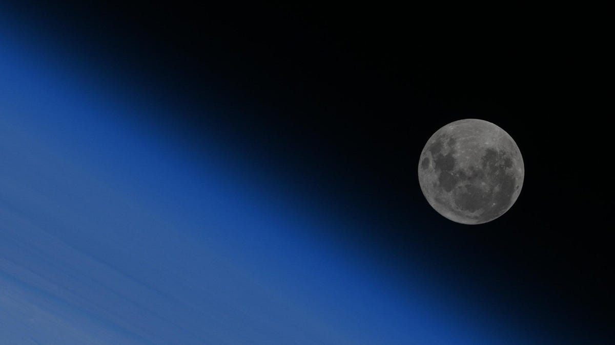 Large blue and cloudy expanse of Earth with full moon in the upper dark corner.