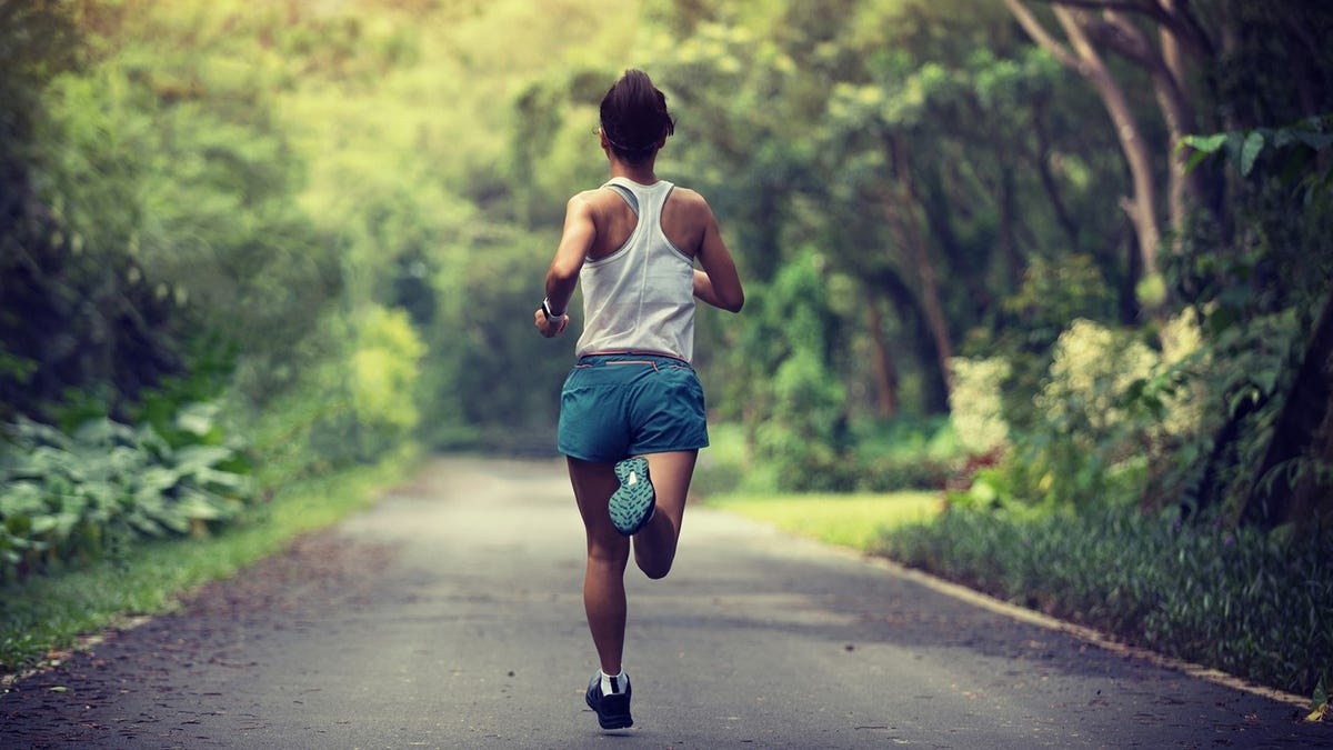 A lone woman runs down a sunny road surrounded by greenery