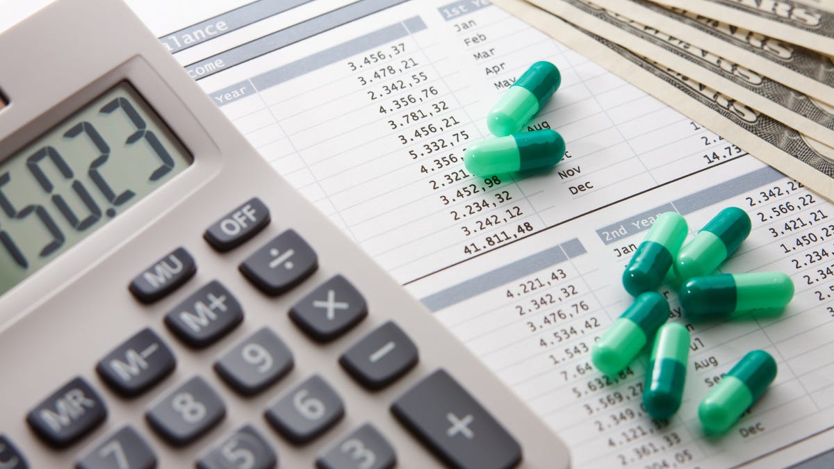 calculator on top of medical bill with green pills and money