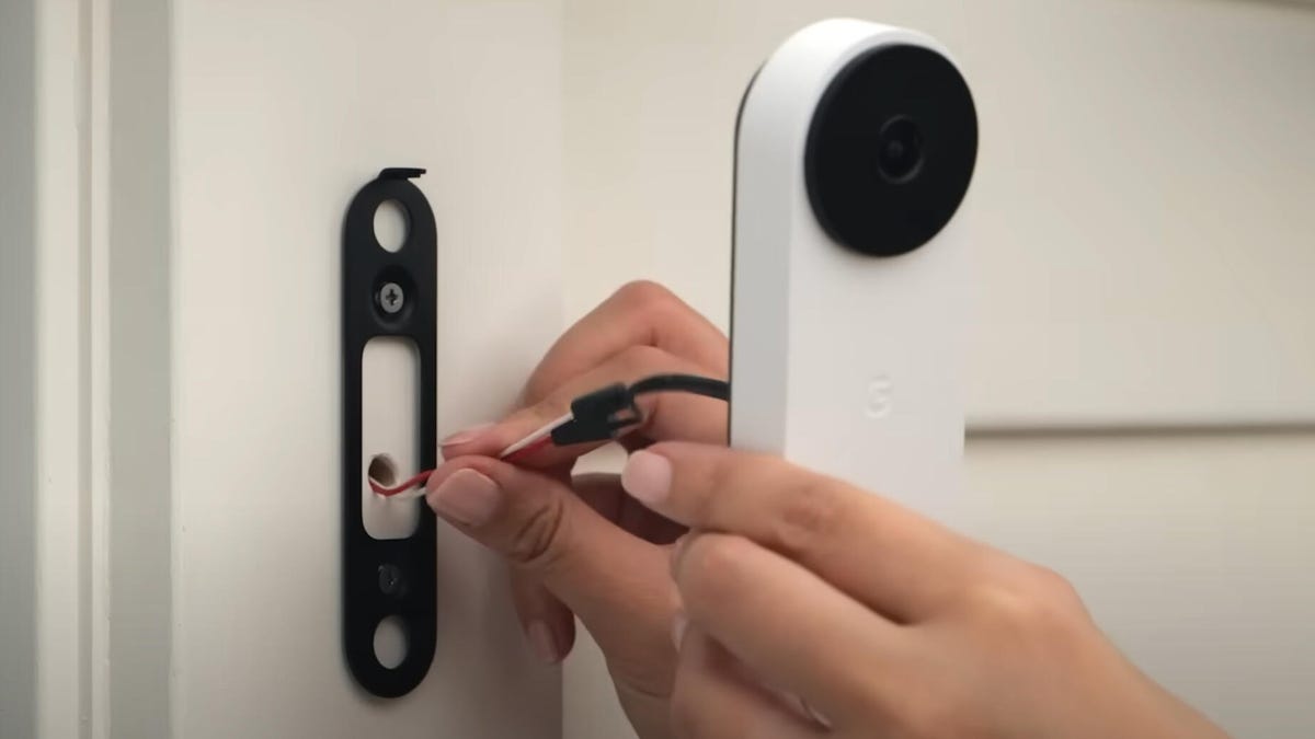 Hands attach doorbell wiring next to a white wall and a white Nest wired doorbell.