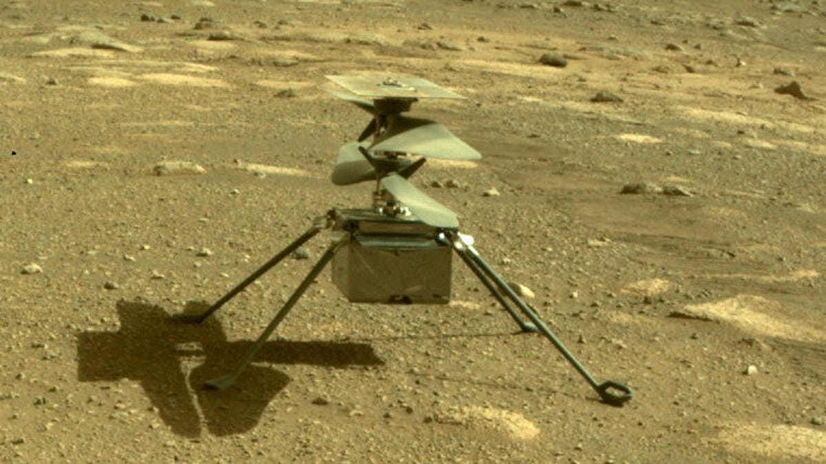 Small Ingenuity helicopter with four legs outstretched and a box-like body sits on the rocky surface of Mars.