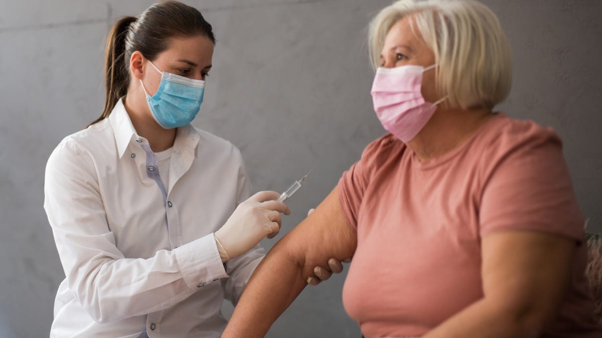 A woman in a pink shirt gets vaccinated by a doctor
