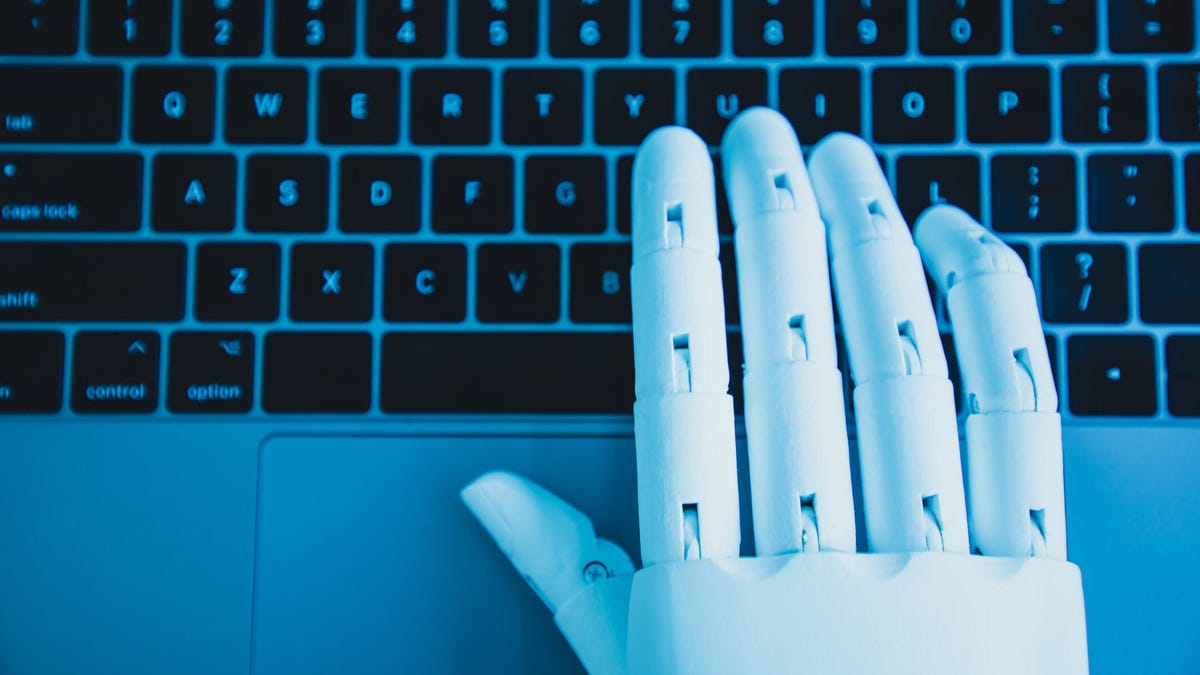 A robotic hand types on a laptop keyboard.