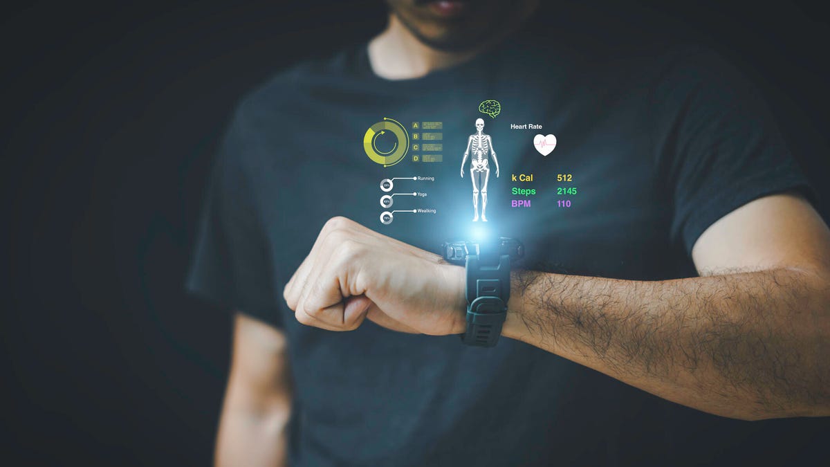 A man looks a wrist device with illustrations of health data floating in the air.