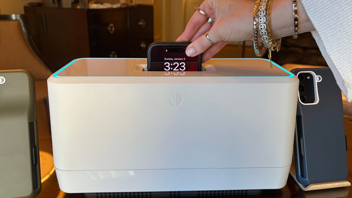 An iPhone being inserted into the top of a large, white box.