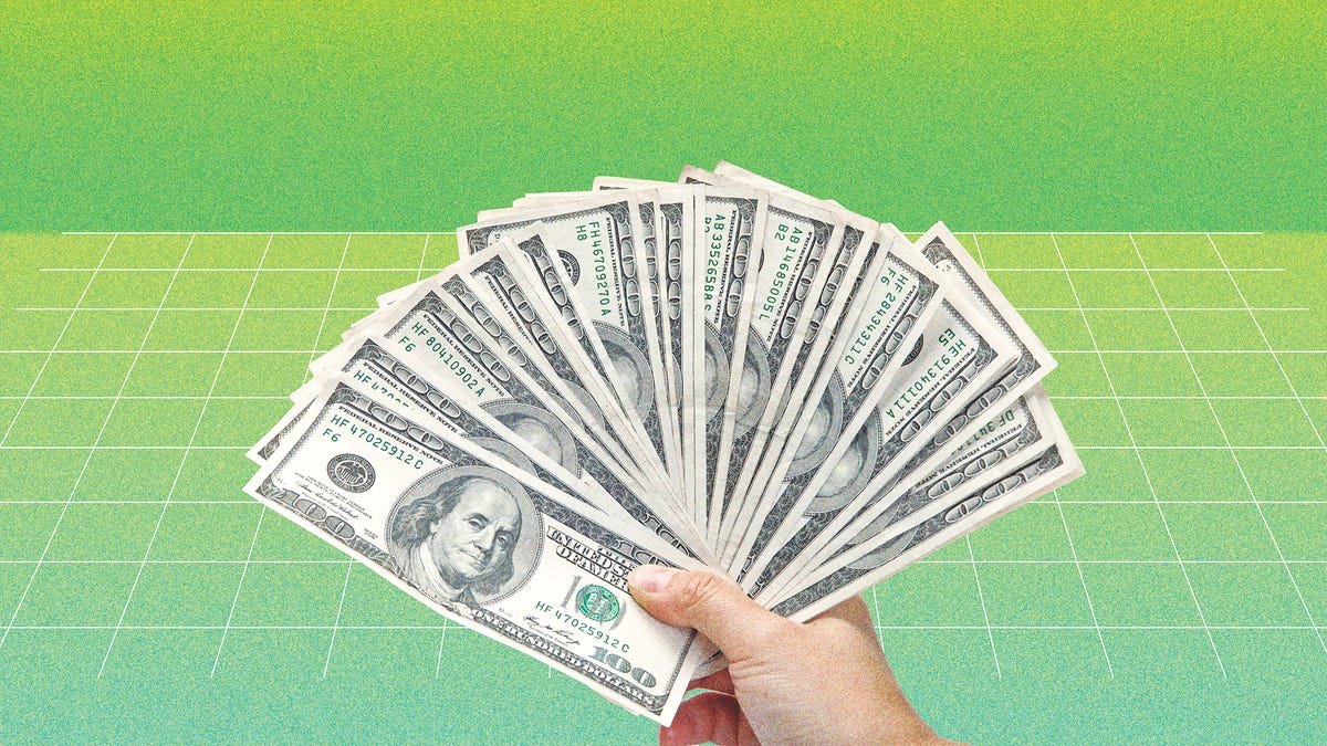 hand holding a fan of money across a green background