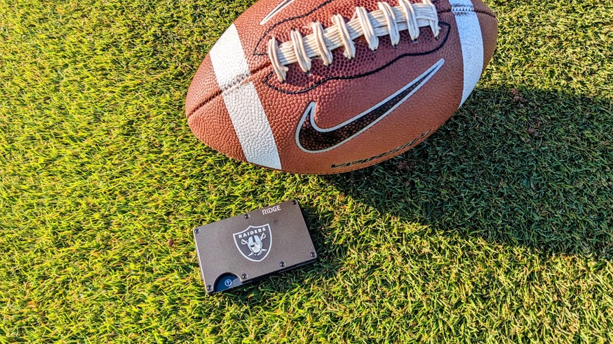 A black metal wallet on the grass with an American football next to it