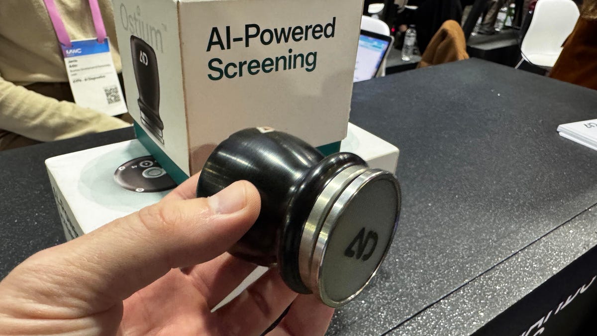 A handheld gadget, which looks like a pizzeria salt pepper flakes shaker, is held up in front of product boxes.