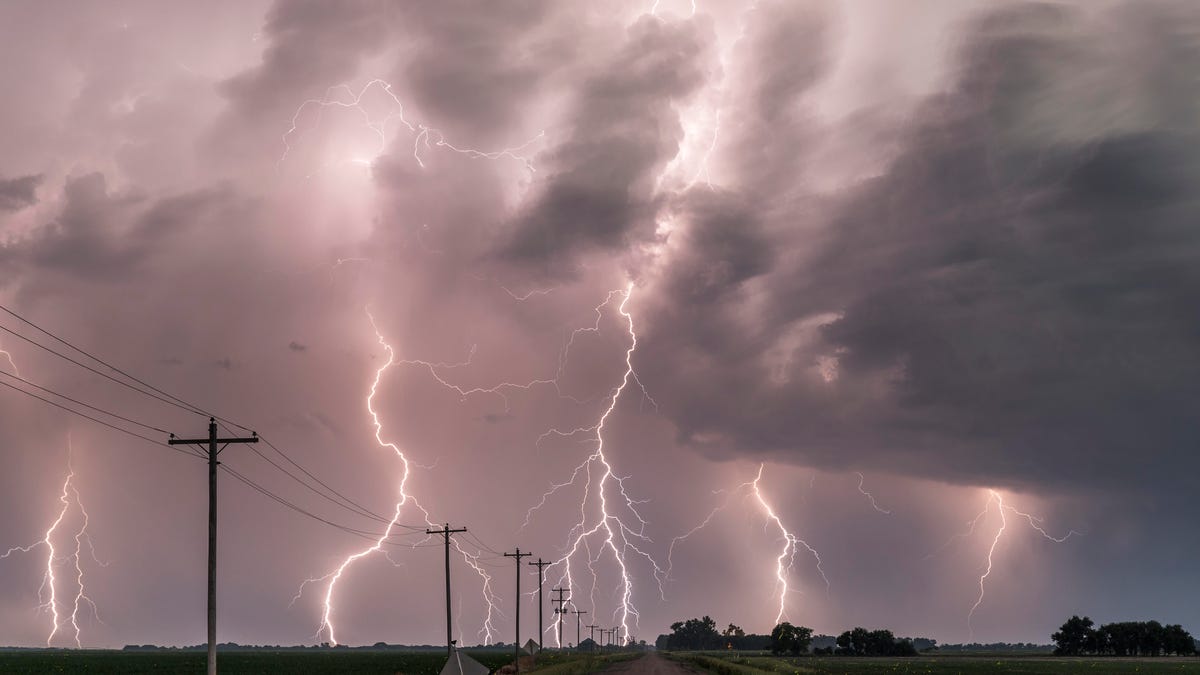 a thunderstorm with multiple lightning strikes over a rural road