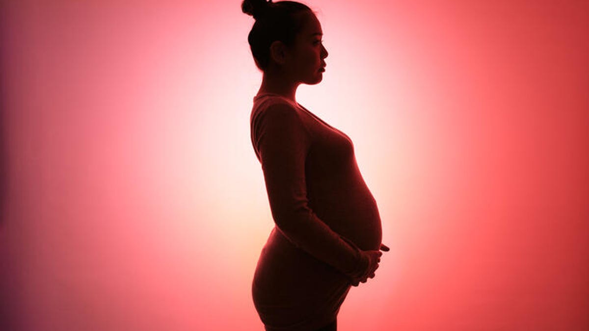 Side profile of a pregnant woman standing in front of a red background.
