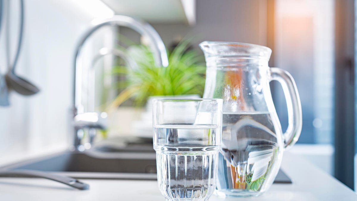 A pitcher of water and a glass by a kitchen sink.