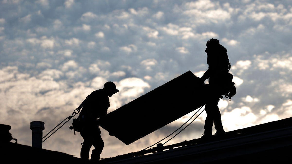 Silhouettes of people installing solar panels on a rooftop.