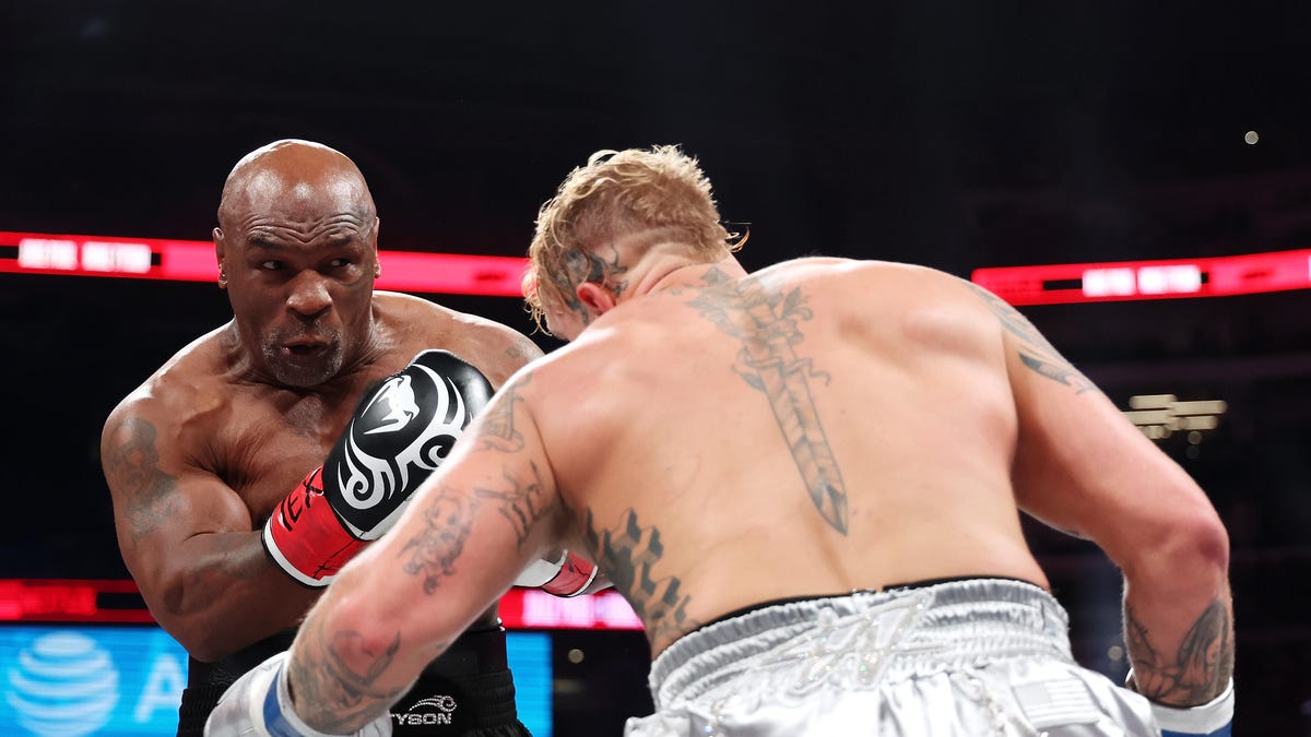 Mike Tyson ducks to his right while prepared to punch Jake Paul, whose back is to the camera