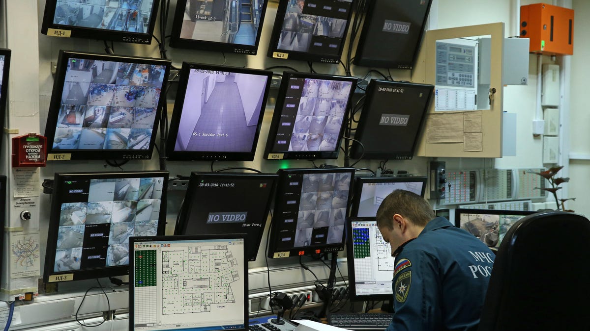 A security official sits in front of a bank of 12 camera monitors