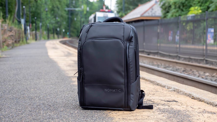 Nomatic Travel Backpack sitting on the ground next to railroad tracks