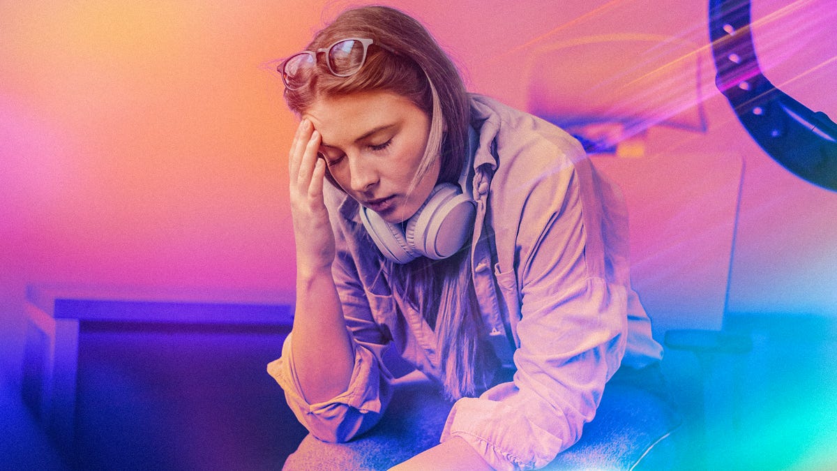 A woman with headphones on her neck holds her head.