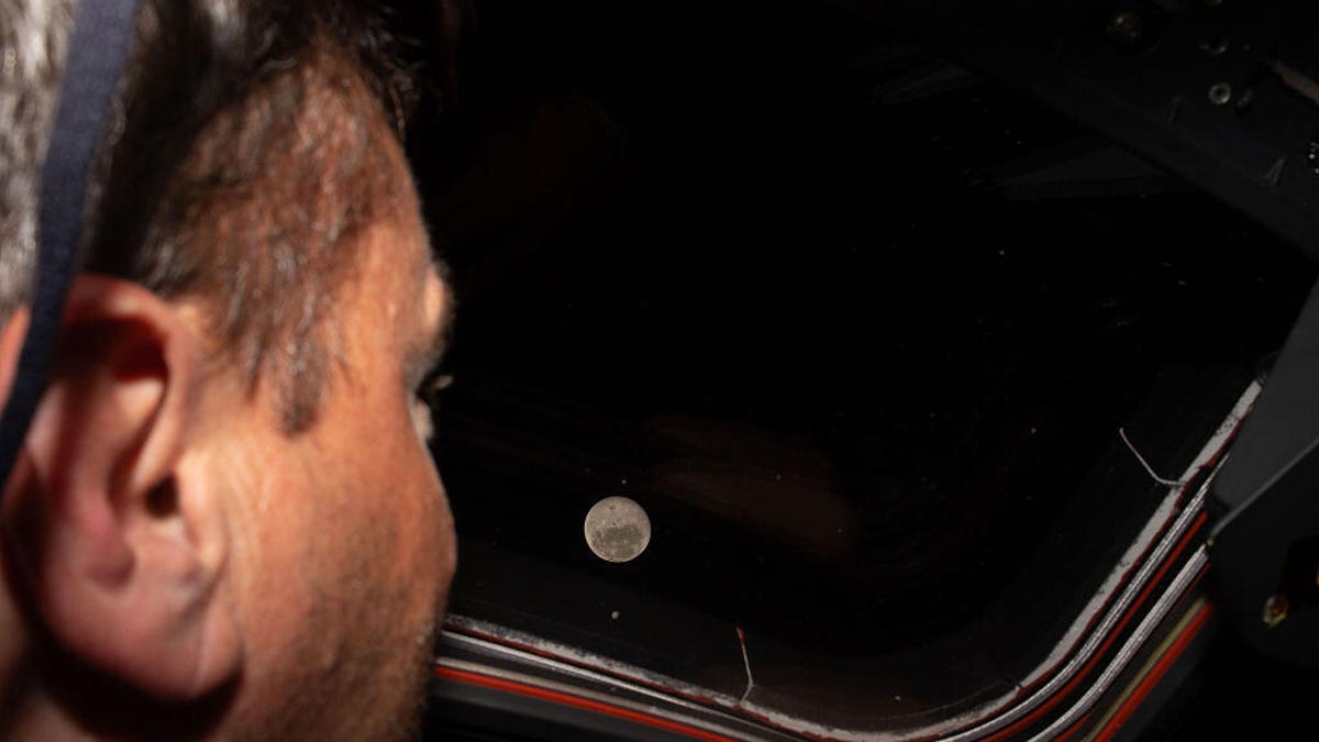 an astronaut looks out a window at the moon in the distance