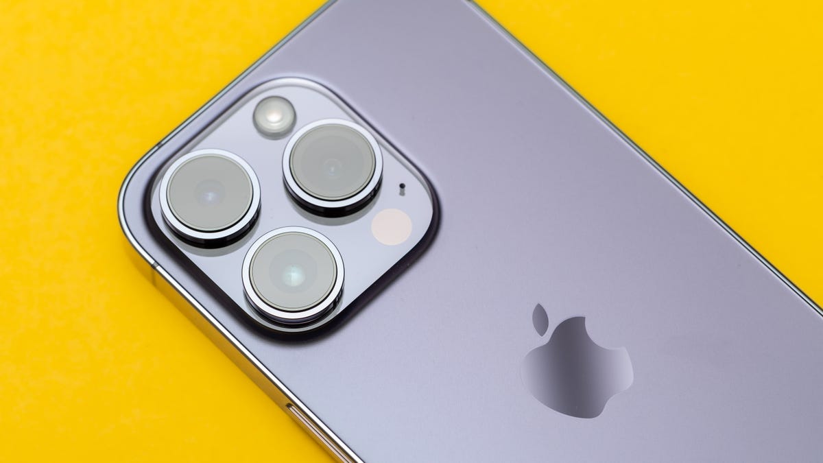 A deep purple iPhone 14 Pro with three cameras pointing upward lies on a yellow background