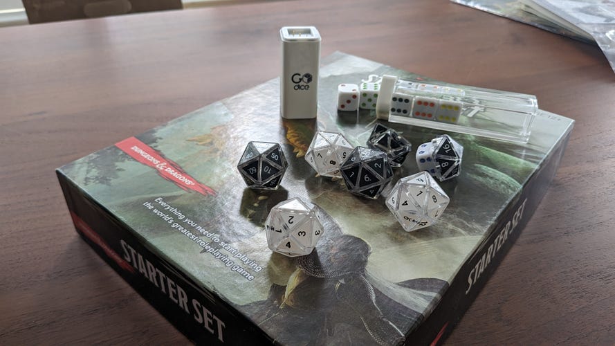 A set of polyhedral dice and a set of 6 sided dice on a D&D box