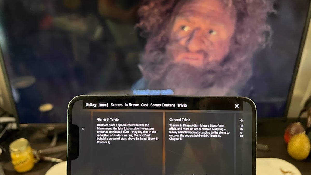 Rings of Power male character in background with smartphone with trivia about the show in the foreground