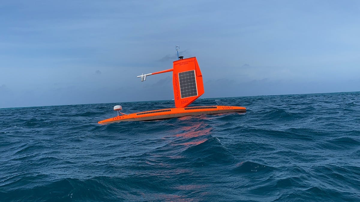 An orange drone ship floats on quiet ocean waves.