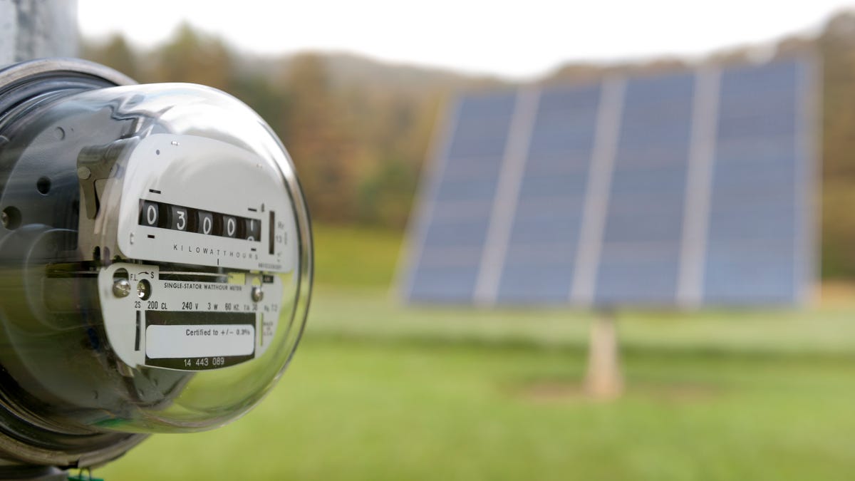 An electricity meter with solar panels in the background.