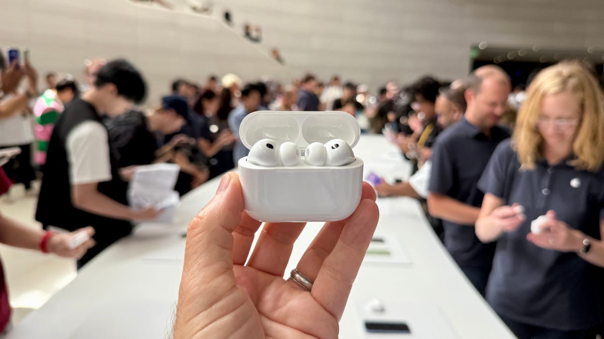 airpods pro 3 being held by fingers in a crowd of people around a long white table