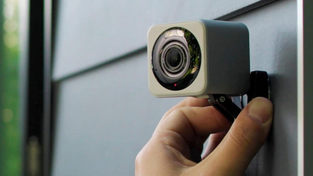 A hand adjusts a Wyze cam on exterior siding.