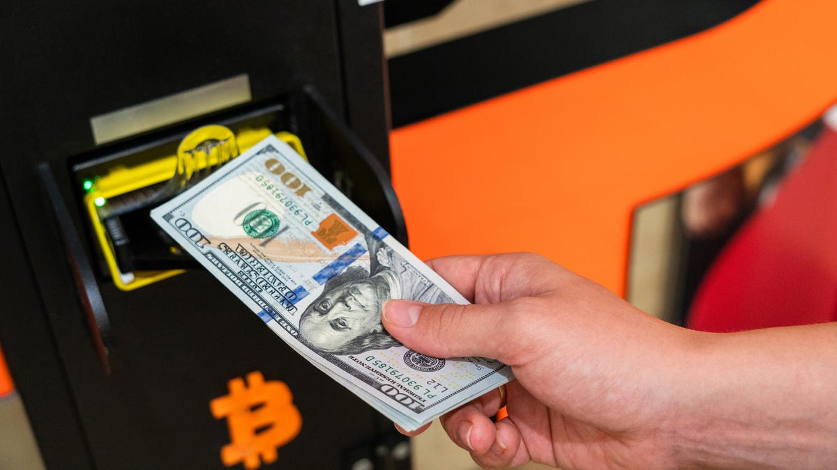 An image of a hand feeding cash ito a Bitcoin ATM.