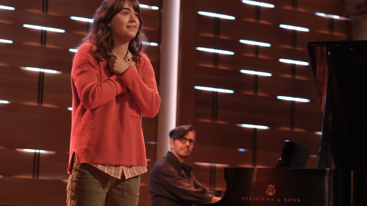 A young woman sings on stage with her arms crossed over her heart