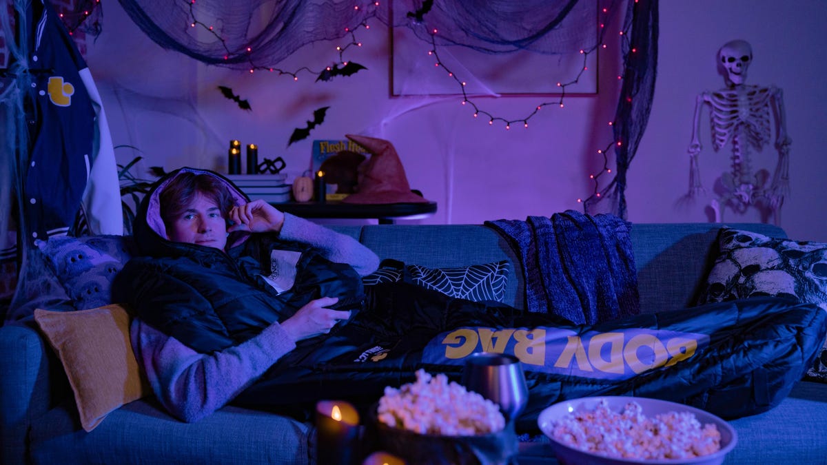 man reclined on couch with sleeping bag surrounded by halloween decor