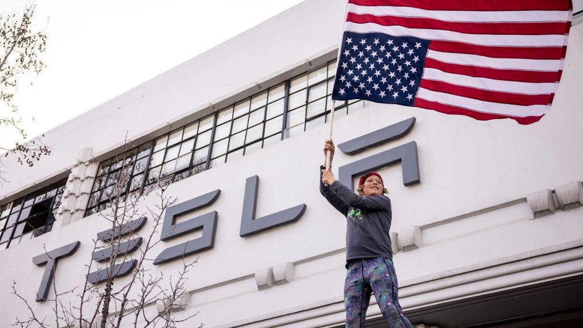A boy waves an upside-down American flag outside a Tesla dealership.