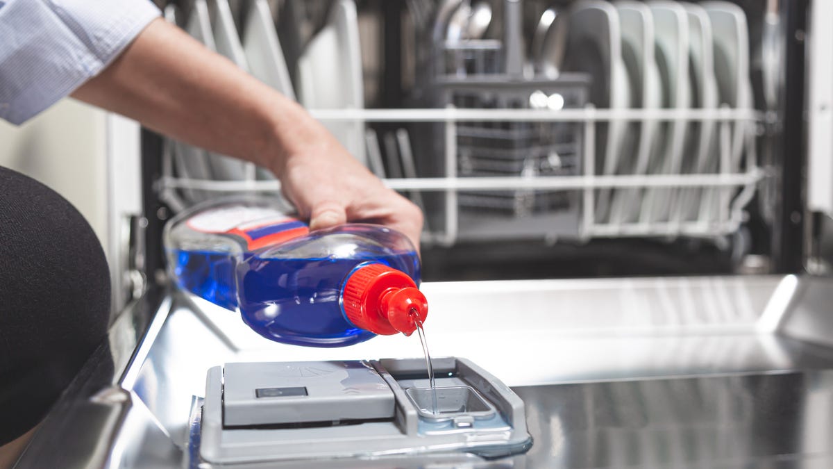 Close-up hand filling dishwasher with gloss liquid into the dishwasher box.