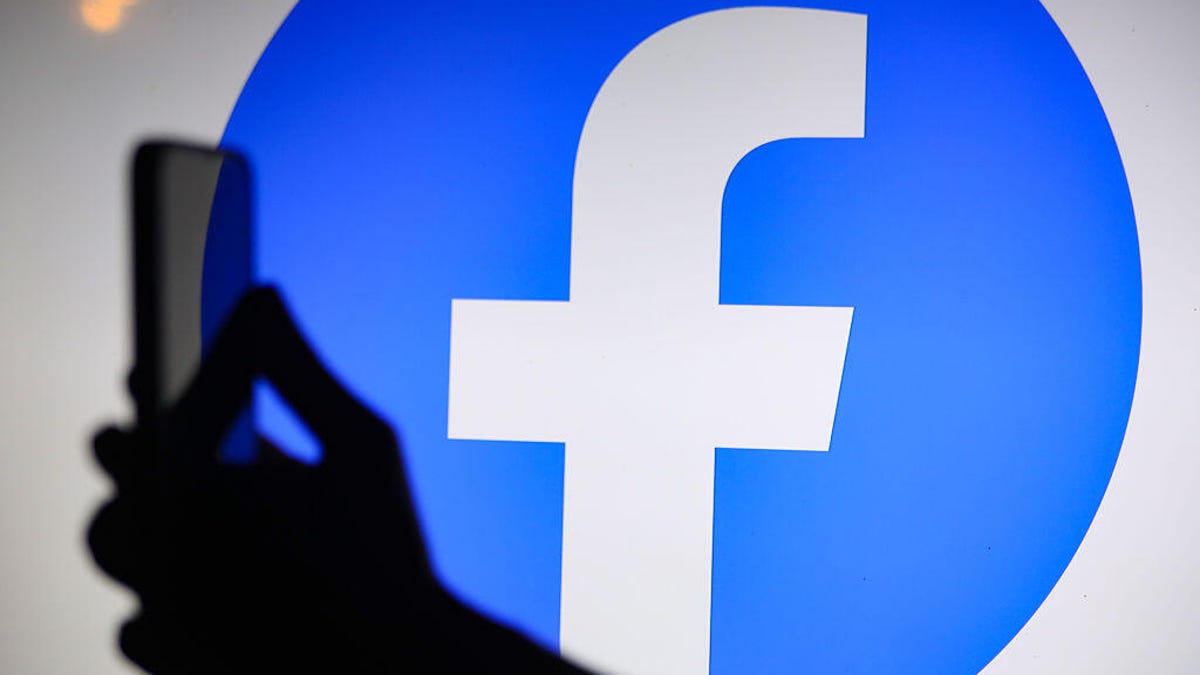 The Facebook logo displays on a screen behind a person holding a phone.