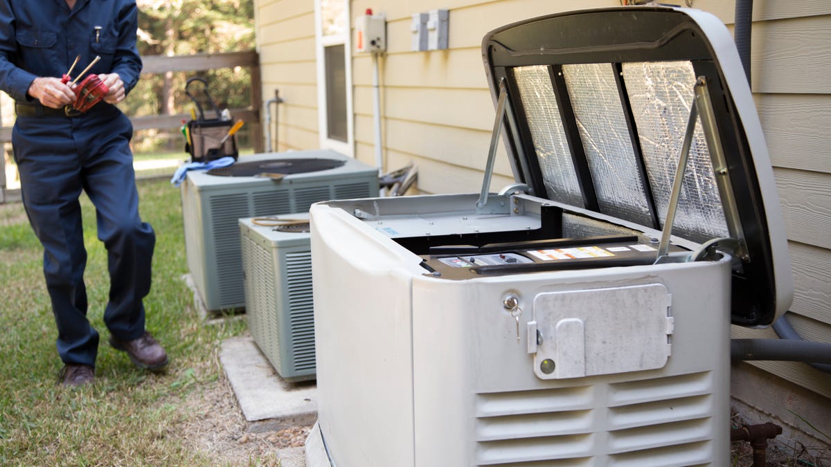 A technician services a generator next to air conditioning units.