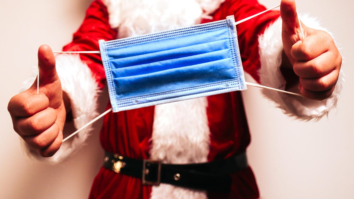 A costumed santa holding out a disposable surgical mask