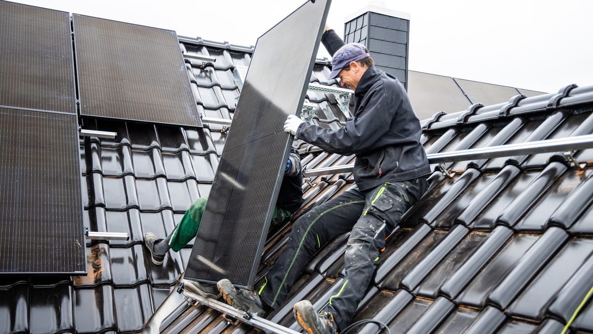 Solar installers mount solar panels on top of a house.