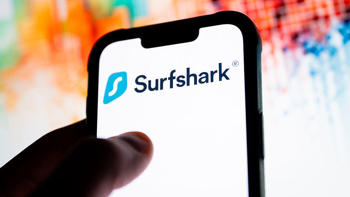 A hand holds a phone with a white screen and Surfshark logo.