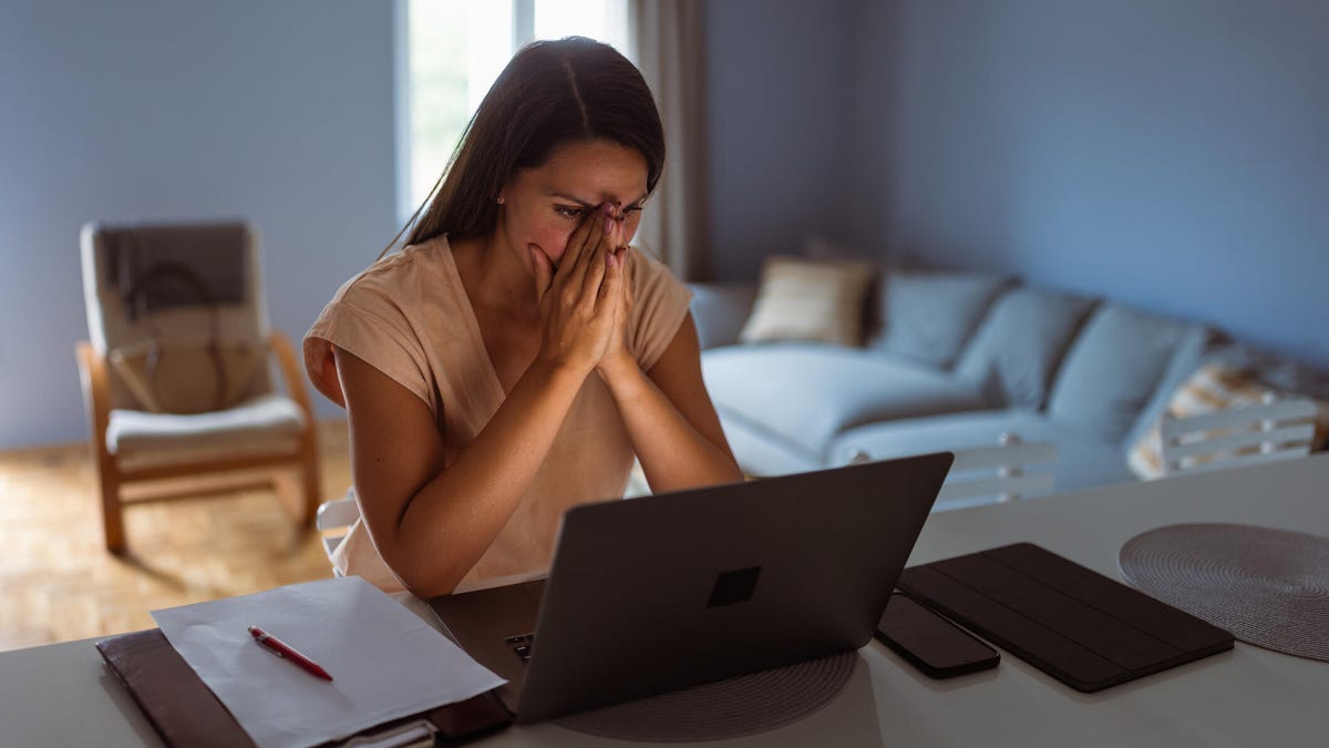 An image of a worried-looking woman sitting at a laptop.