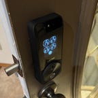 A Lockly Visage lock with keypad glowing on an open brown door.