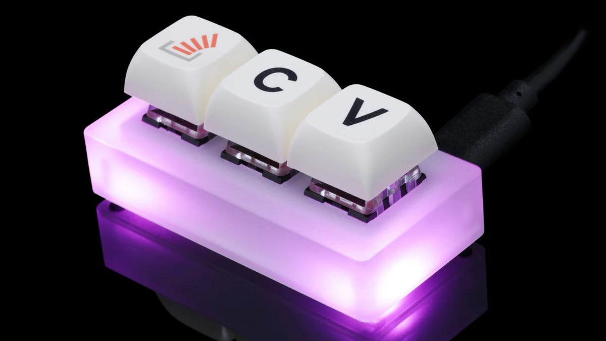 A three-key tiny keyboard with a bright RGB-lit opaque base on a black, reflective surface.