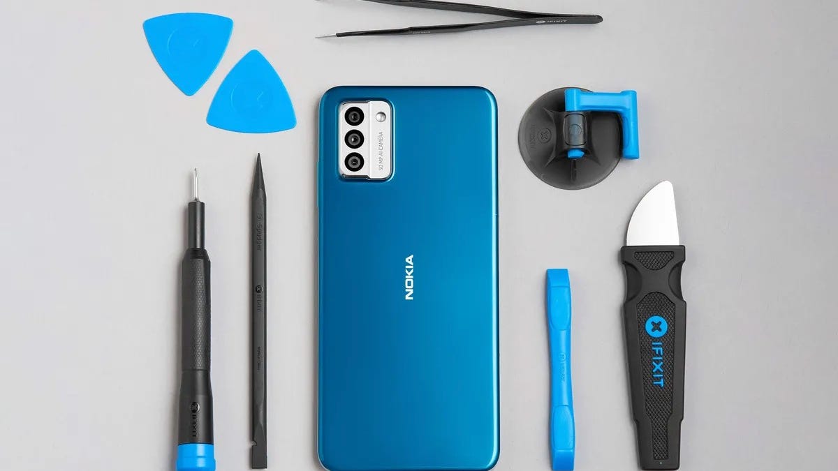 A cyan-blue Nokia G22 is surrounded by an orderly arrangement of various blue and black implements, including a large scalpel-like knife, a pair of tweezers and what look like a couple of guitar picks.