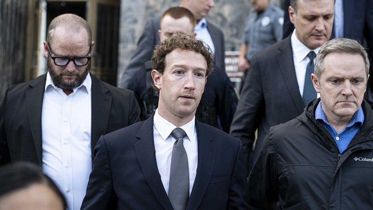Mark Zuckerberg, founder of Meta, stands outside a courtroom wearing a business suit. He is surrounded by other unidentified people.