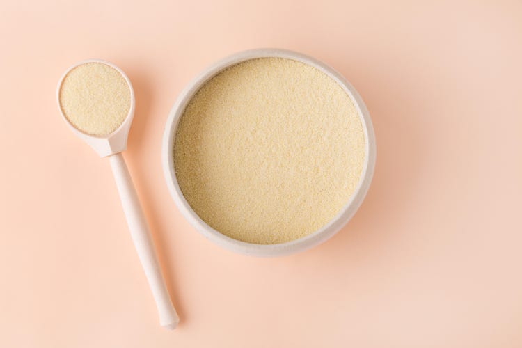 A spoonful of collagen powder against a light pink background 