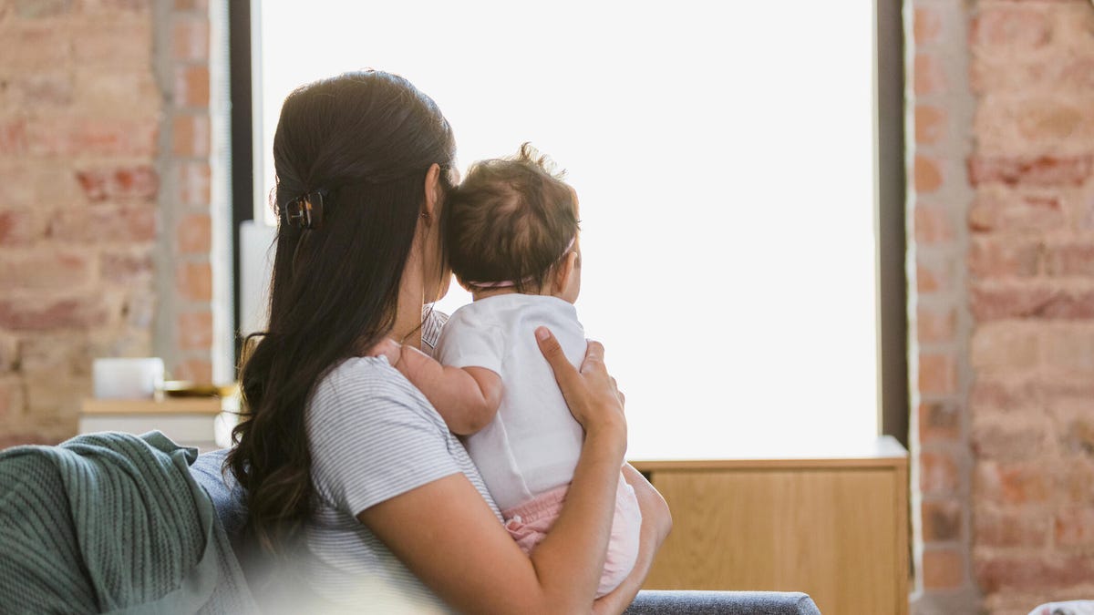 A mother holds her baby and they both look out the window