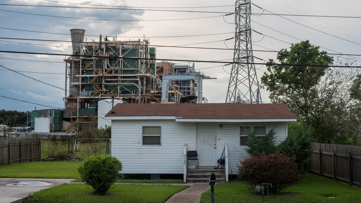 A house sits along a stretch of road dubbed "Cancer Alley," with an industrial plant in the background.