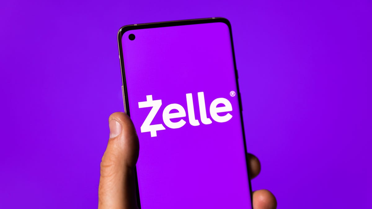 A person holds a phone with the Zelle logo on it