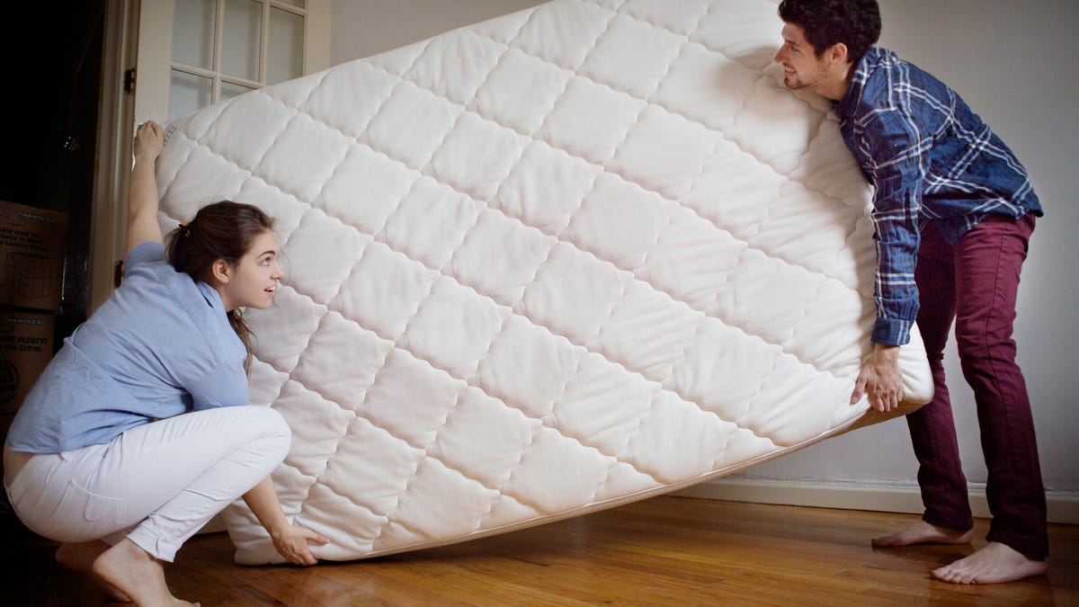 Couple carrying mattress in room