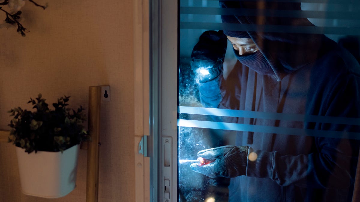 A burglar with a flashlight tinkers with a house door.