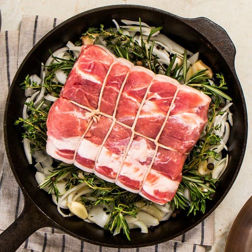 a black cast iron pan with herbs and a pork loin